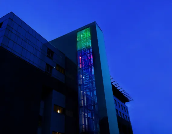 Abendblauer Himmel kurz vor Dämmerung und davor ein Gebäude mit sichtbar beleuchtetem Fahrstuhlschacht. 