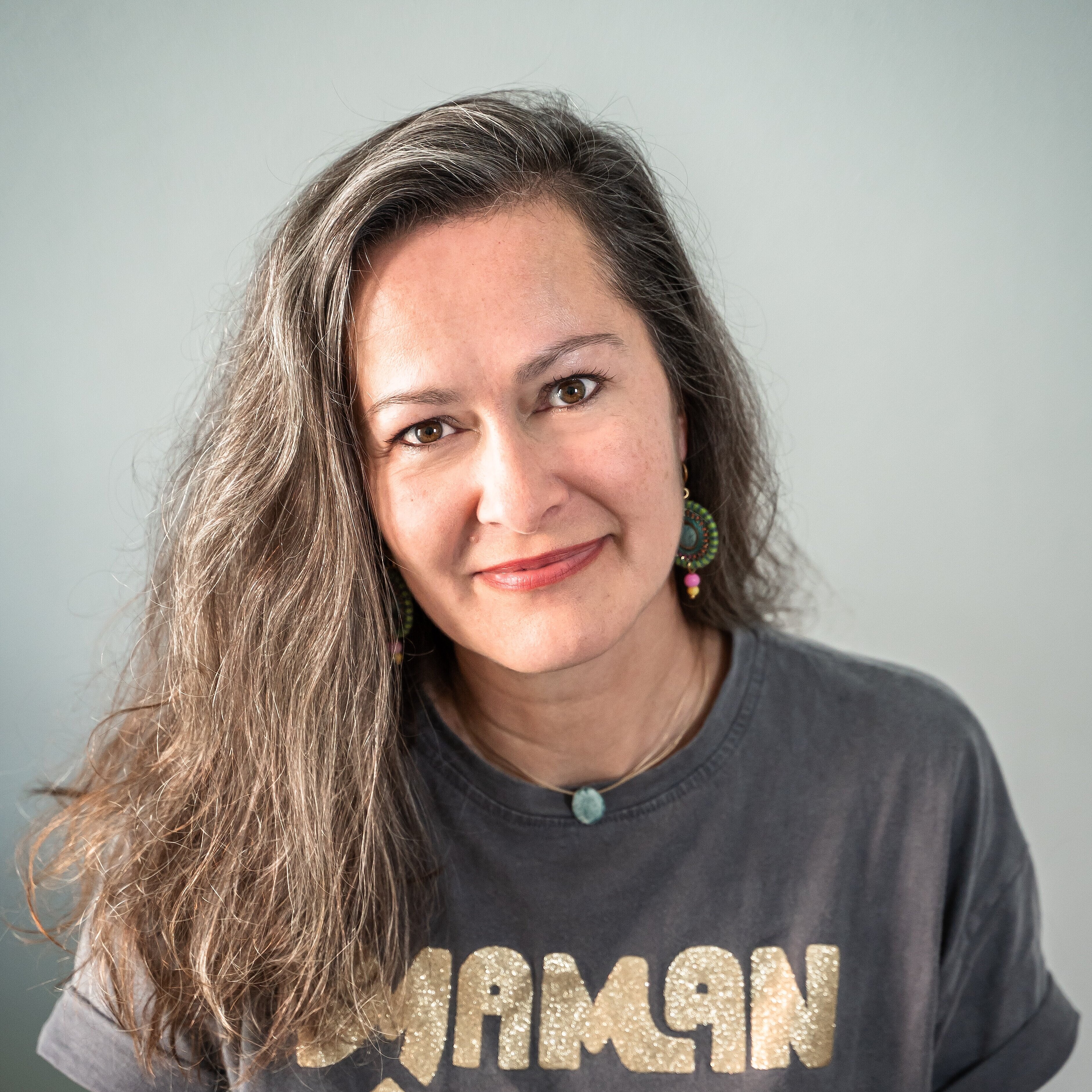 Frau mit langen, gewellten Haaren trägt ein dunkelgraues T-Shirt mit goldener Aufschrift 'MAMAN D'AMOUR'