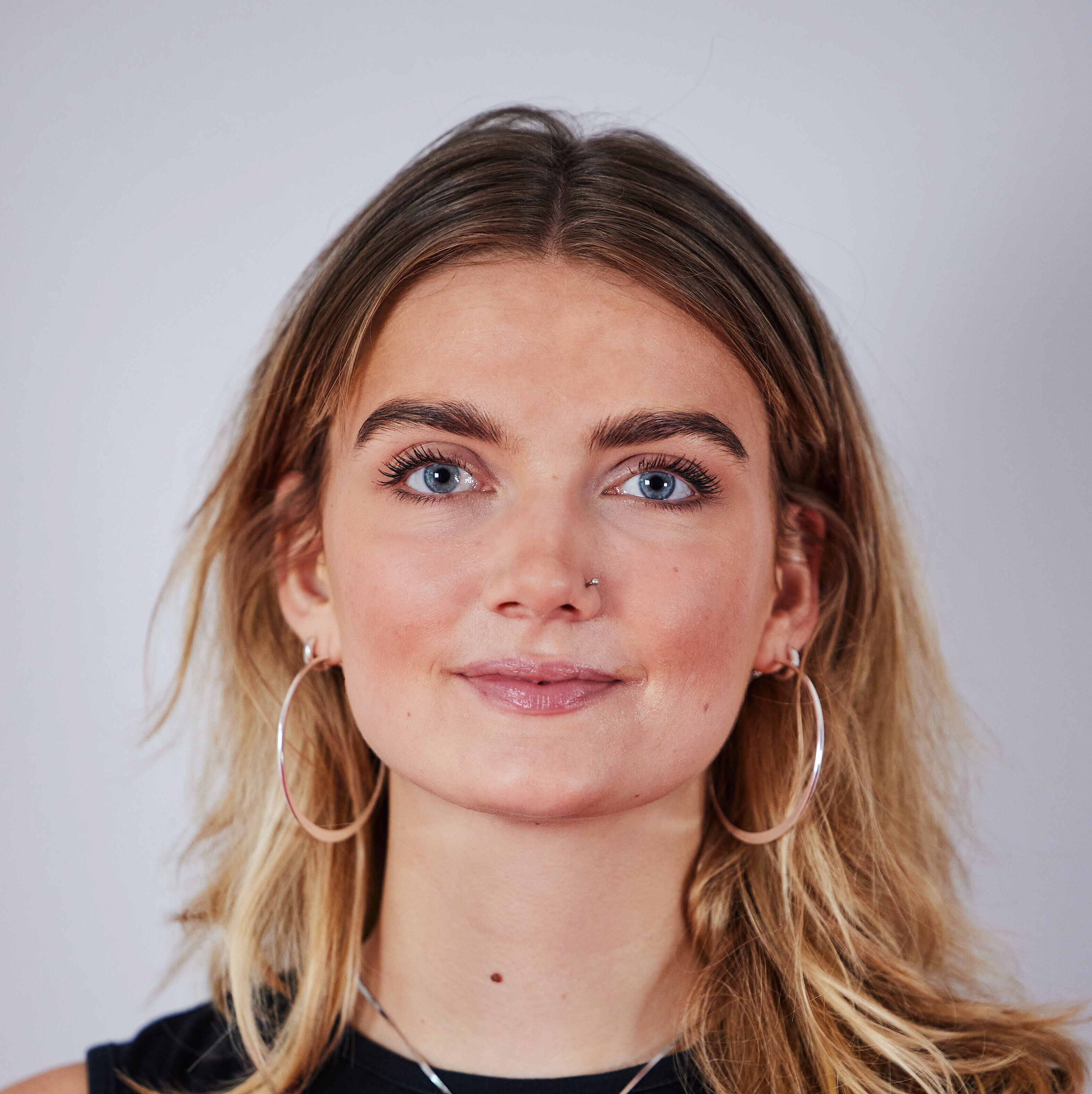 Frau mit schulterlangen blonden Haaren, trägt schwarzen Ärmellosen Pullover mit rotem Muster, großen silbernen Creolen.