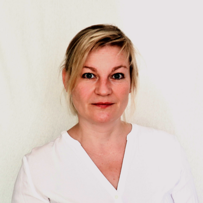 Frau mit hochgestecktem blonden Haar trägt ein weißes Oberteil mit V-Ausschnitt vor hellem Hintergrund