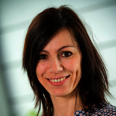 Frau mit schulterlangem braunem Haar vor unscharfem Hintergrund