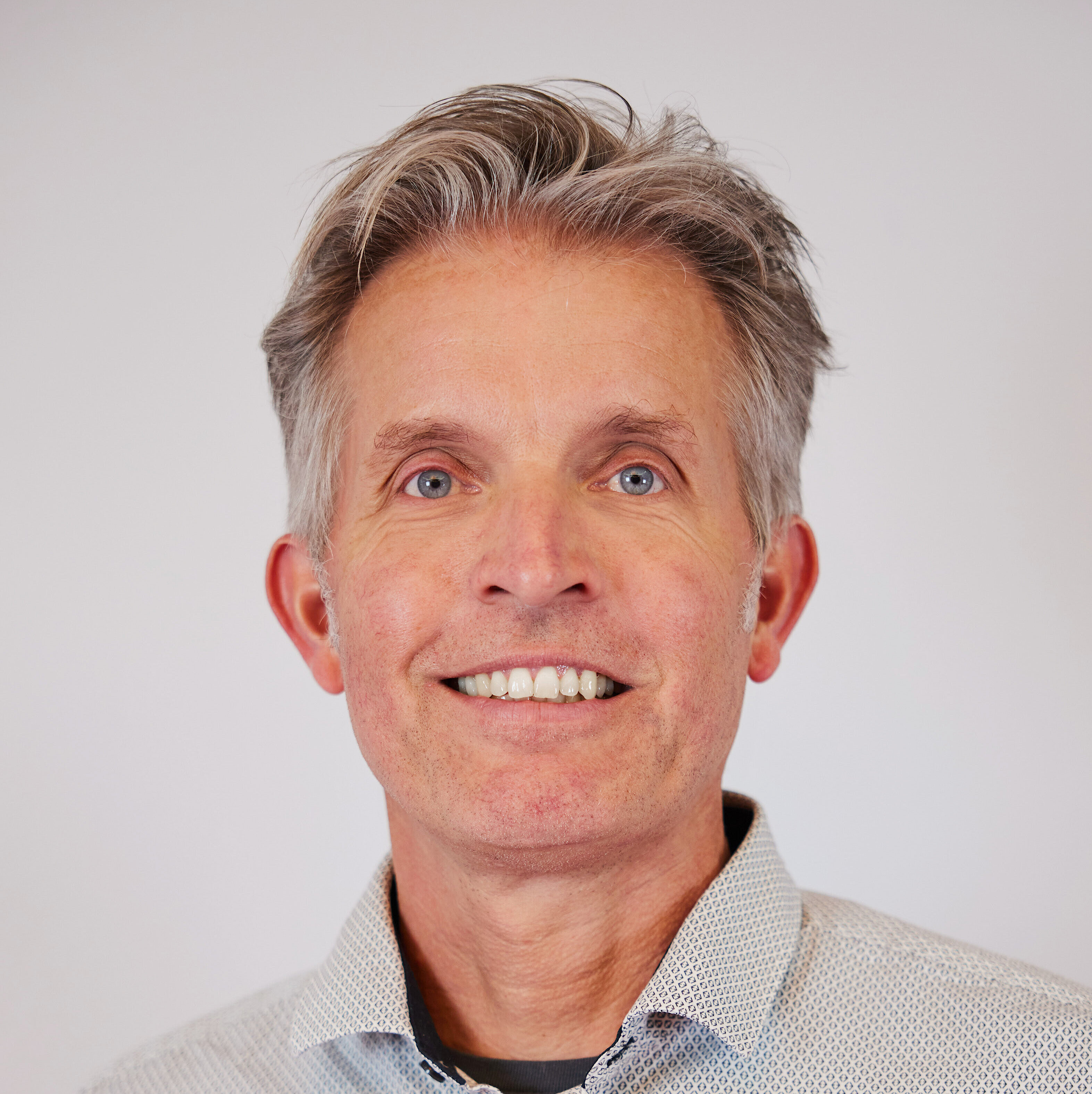 Mann mit grauen Haaren, Hemd mit feinem Muster und offenem Kragen, vor hellem Hintergrund