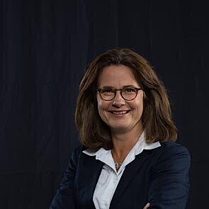 Frau mit schulterlangem braunem Haar, schwarzem Blazer, weißer Bluse.