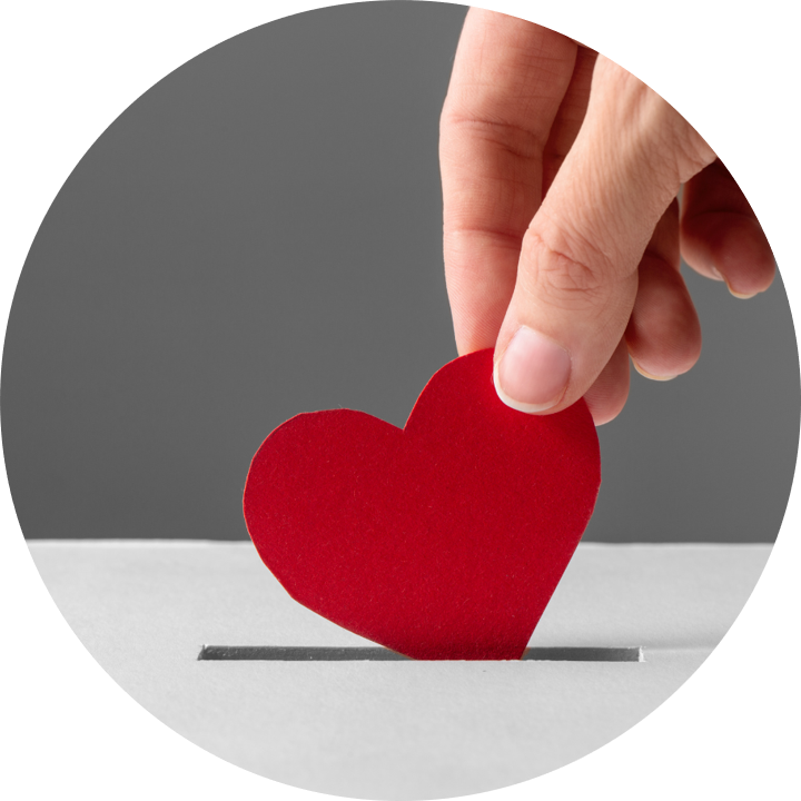 Eine Hand steckt ein rotes Herz aus Papier in einen Schlitz auf einer Oberfläche.