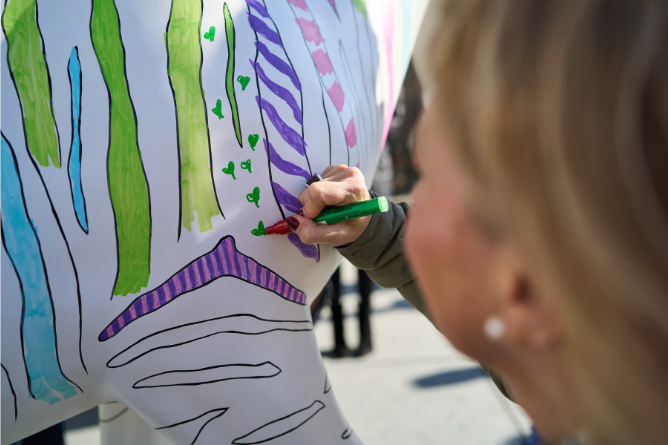 © Stefan Schubert Frau malt mit grünem Stift kleine grüne Herzen auf eine weißgrundige Skulptur mit bunten Streifen und Mustern
