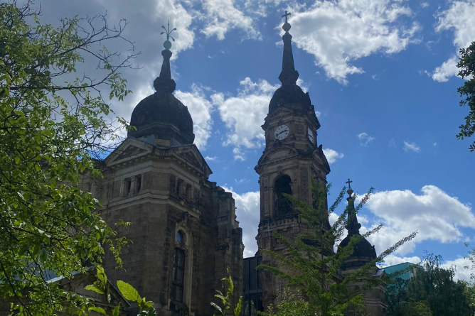 Sommer, Sonne und Seltene Blick auf zwei hohe Kirchtürme mit barocker Architektur vor blauem Himmel mit Wolken und umgeben von Bäumen