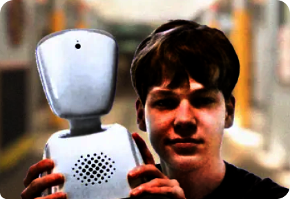 Person hält einen weißen, humanoiden Roboter mit rundem Kopf und Lautsprechergitter auf der Brust vor sich.