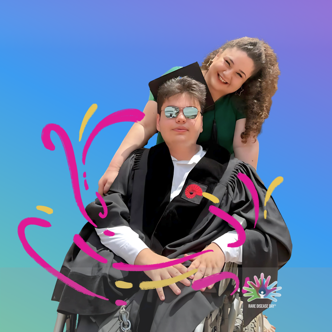 Person im Rollstuhl mit schwarzer Robe und roter Blume am Revers, umarmt von einer weiteren Person mit lockigem Haar vor blauem Himmel, bunte grafische Linien und Rare Disease Day-Logo unten rechts