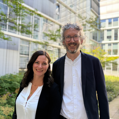 Johanna Schäfer und Prof. Dr. Holger Storf Zwei lächelnde Personen vor einem modernen Bürogebäude, die Frau trägt eine weiße Bluse und der Mann eine Brille und ein dunkles Sakko