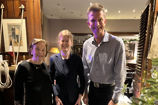 Drei Personen stehen in einem Raum mit Holzvertäfelung und Weihnachtsbaum, zwei Frauen und ein Mann in legerer Kleidung