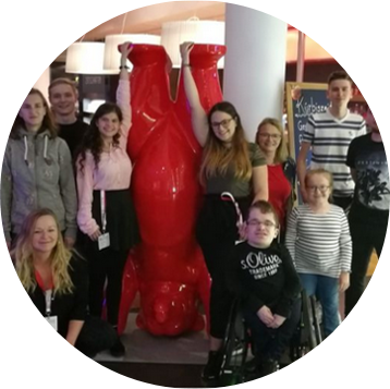 Gruppe von jungen Menschen und Erwachsenen um eine große rote Skulptur einer im Handstand stehenden Bärenfigur in einem Innenraum