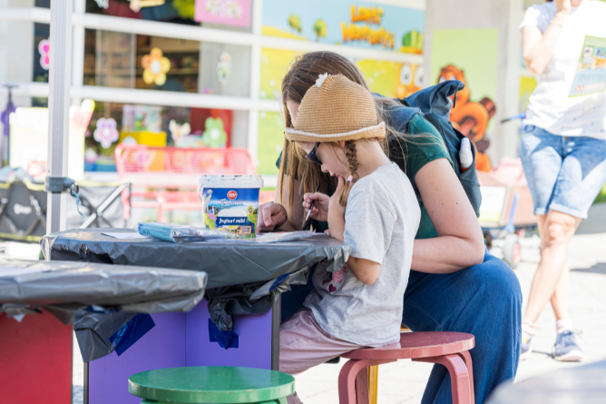 © Ravensburger Spieleland 2026 Kind mit Strohhut sitzt an einem Tisch und spielt mit einer erwachsenen Person im Freien